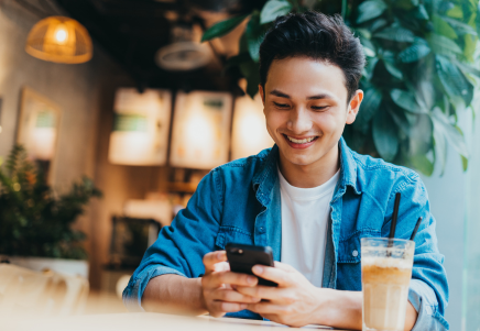 Gen Z Male Smiling At Phone In Coffee Shop