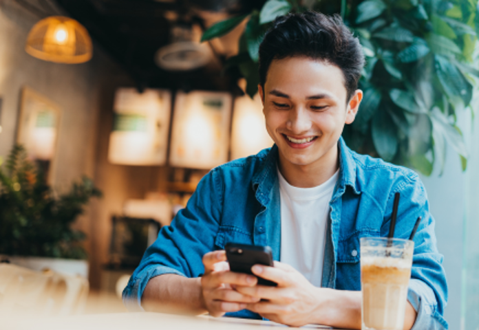 Gen Z Male Smiling At Phone In Coffee Shop