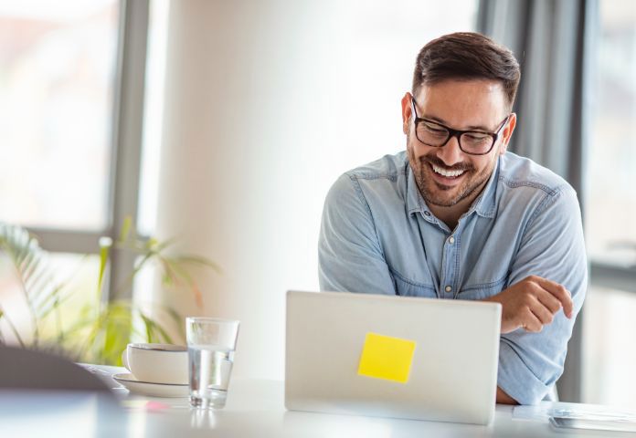 Lächelnder Mann mit einem Laptop, der die Rolle der Technologie bei der Betrugsprävention für die Forderungsfinanzierung von KMU darstellt – Lenvi Insights