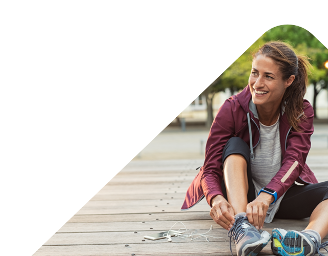 young woman in sportswear smiling and looking off to the right, sat down tying her shoe lace