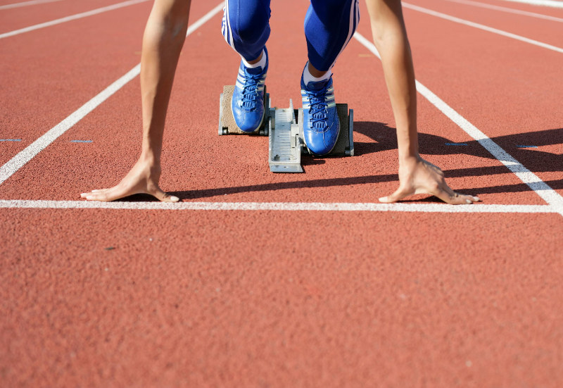 Picture of person in blue sneakers on a starting block on a race track