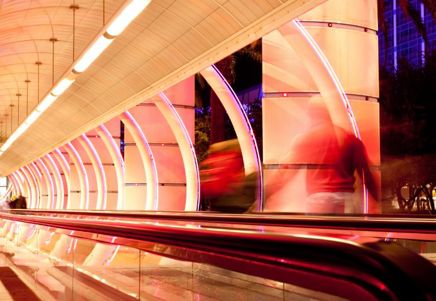 Lenvi image of a white and pink tunnel with a moving walkway and blurred figures