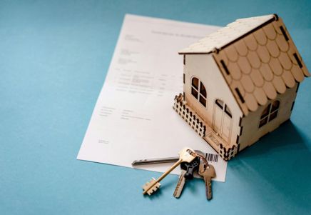 Wooden model house positioned on top of a property document with a set of keys in the foreground, representing mortgage lending, home ownership, and the residential property market