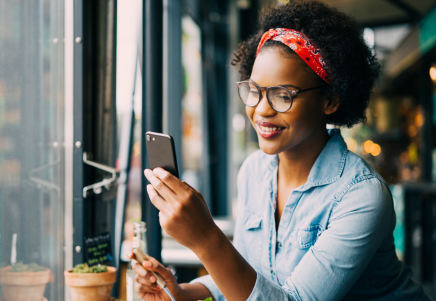 Smiling woman using smartphone in cafe, reflecting Sallyport Commercial Finance's partnership with Lenvi